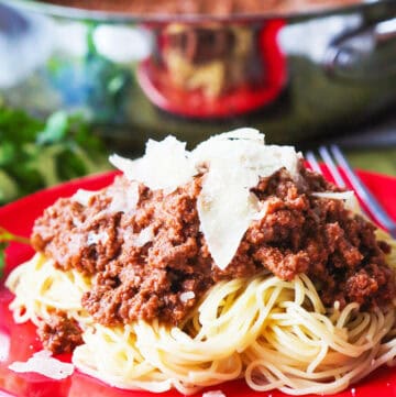 Spaghetti with meat sauce topped with cheese on a red plate.