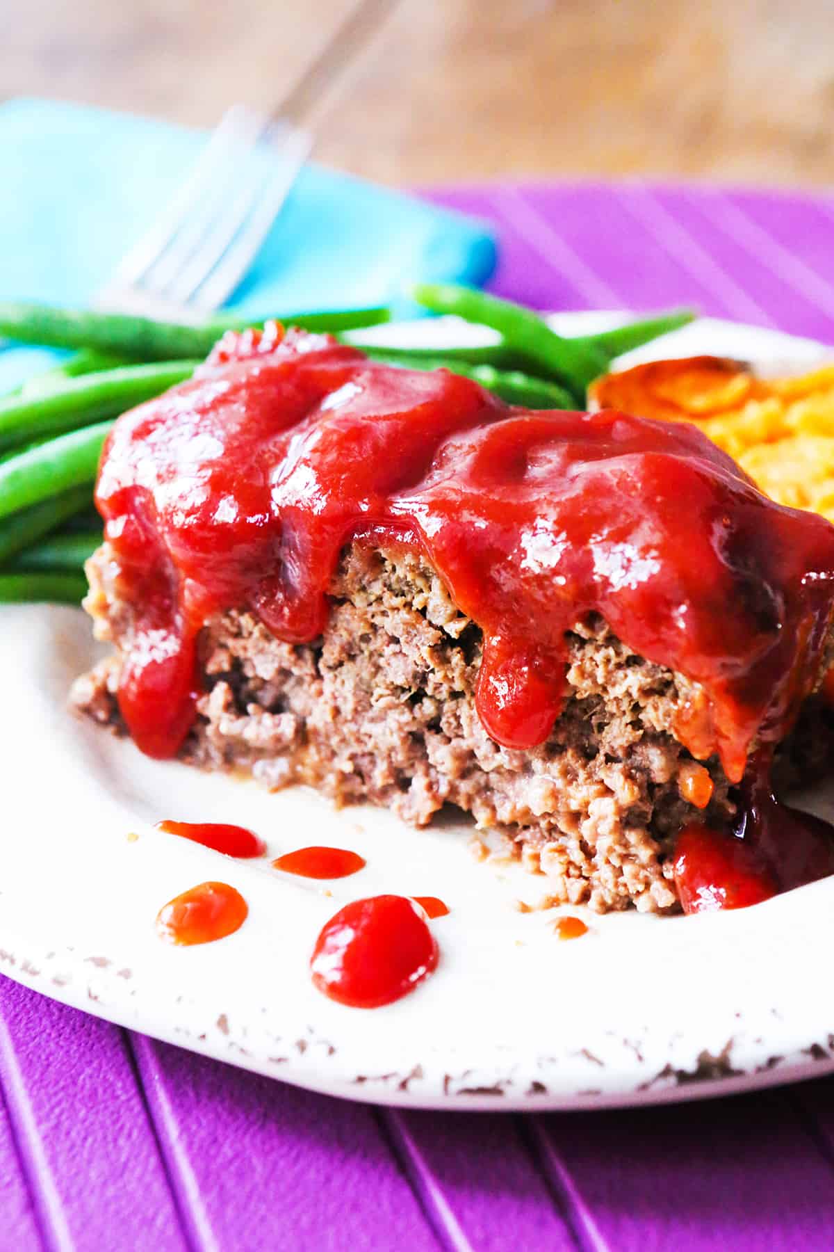 Close-up of meatloaf with ketchup glaze, green beans, and mashed potatoes on a plate.