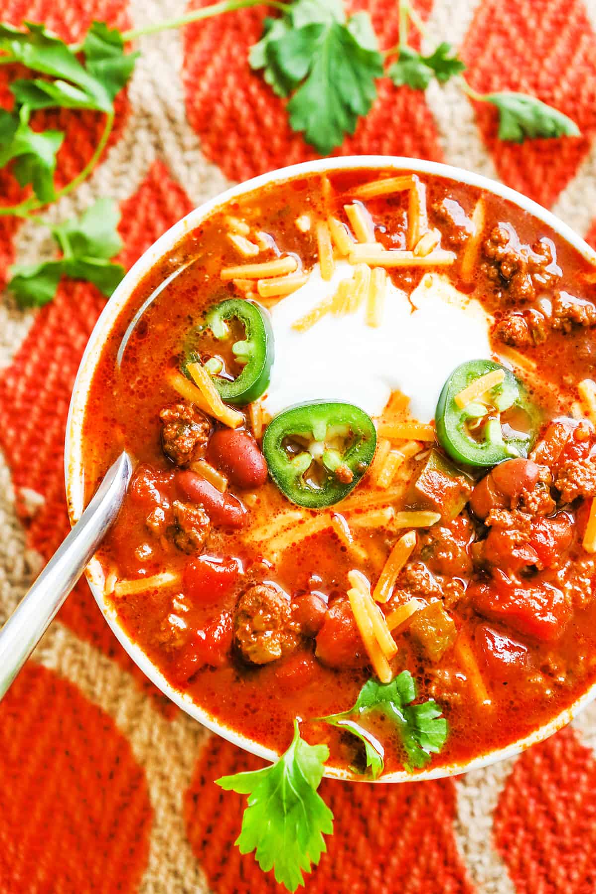 Looking down into a full and hearty bowl of chili topped with jalapeno slices and sour cream.