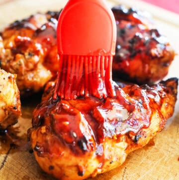 Baked BBQ chicken being glazed with ketchup using a silicone brush.