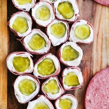 Pickle roll ups with cream cheese and ham on a wooden board.